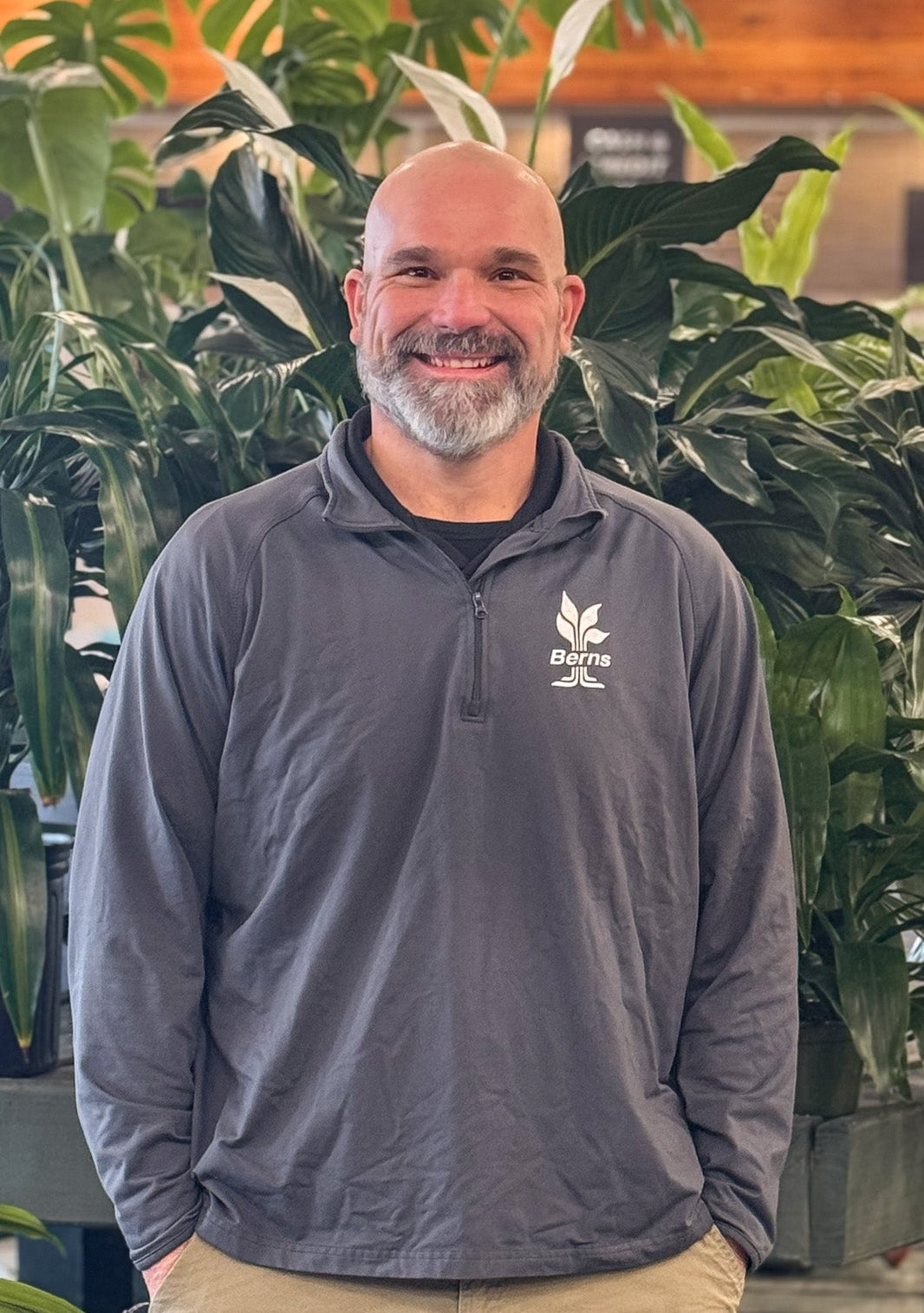 Man wearing a gray jacket with a logo standing among plants