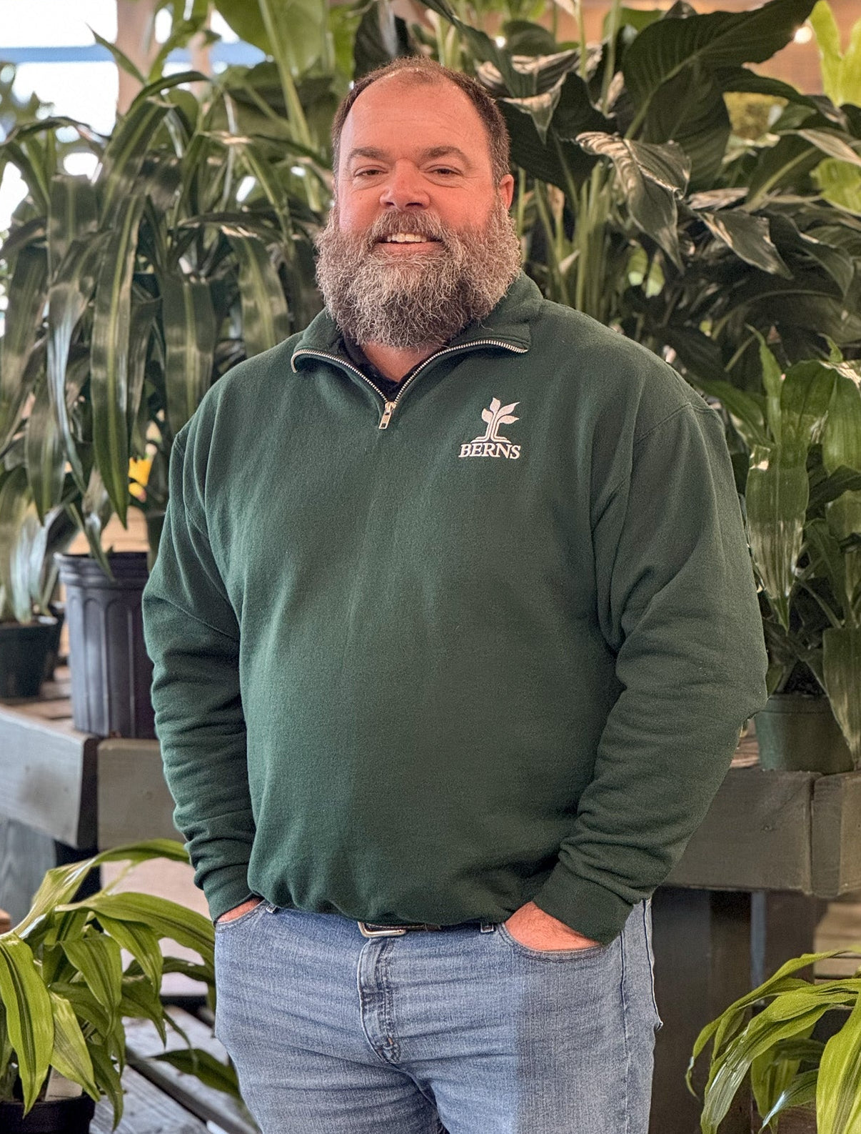 Man in a green sweater standing among plants in a greenhouse