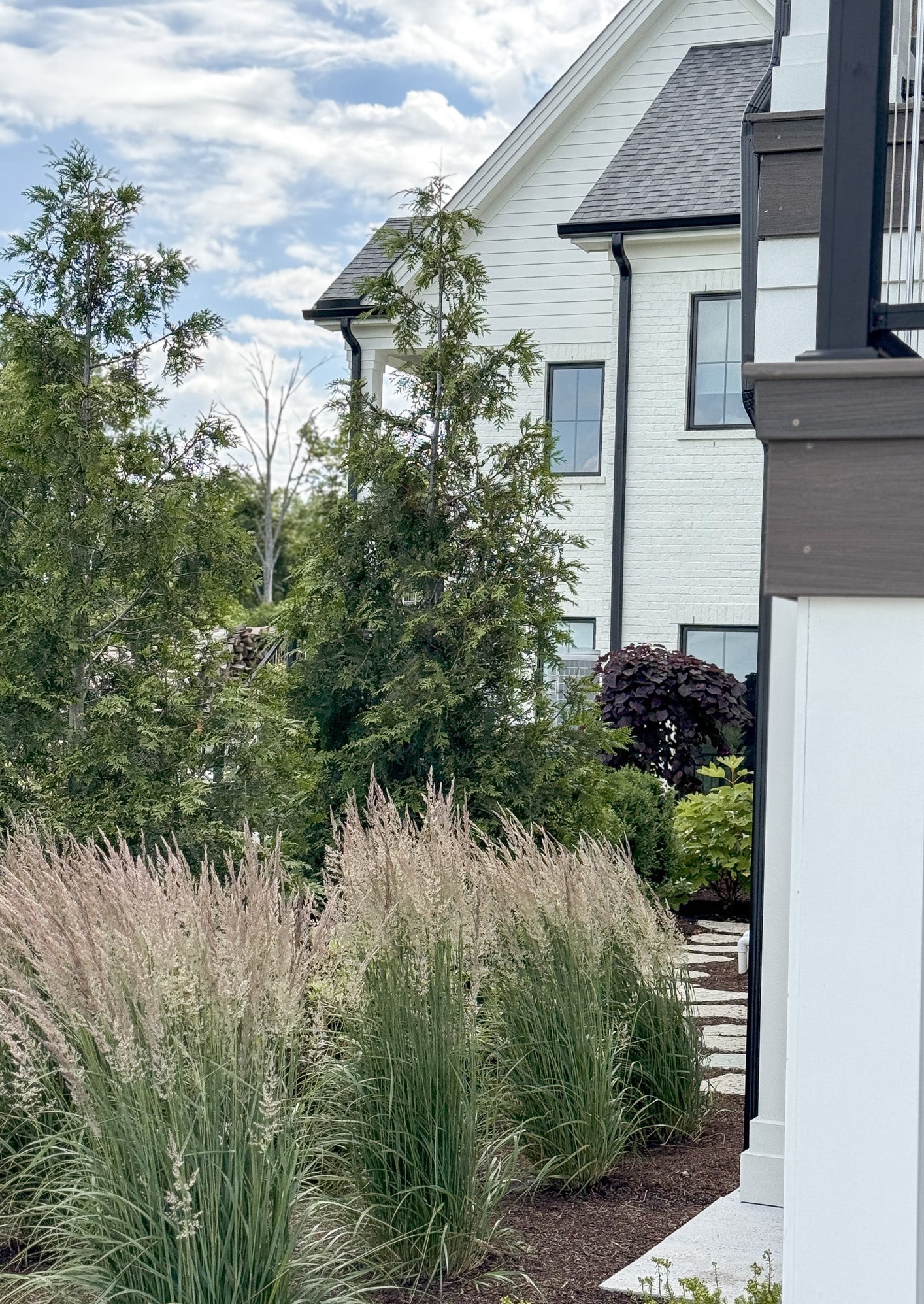 White house with black accents and garden with tall grasses and trees