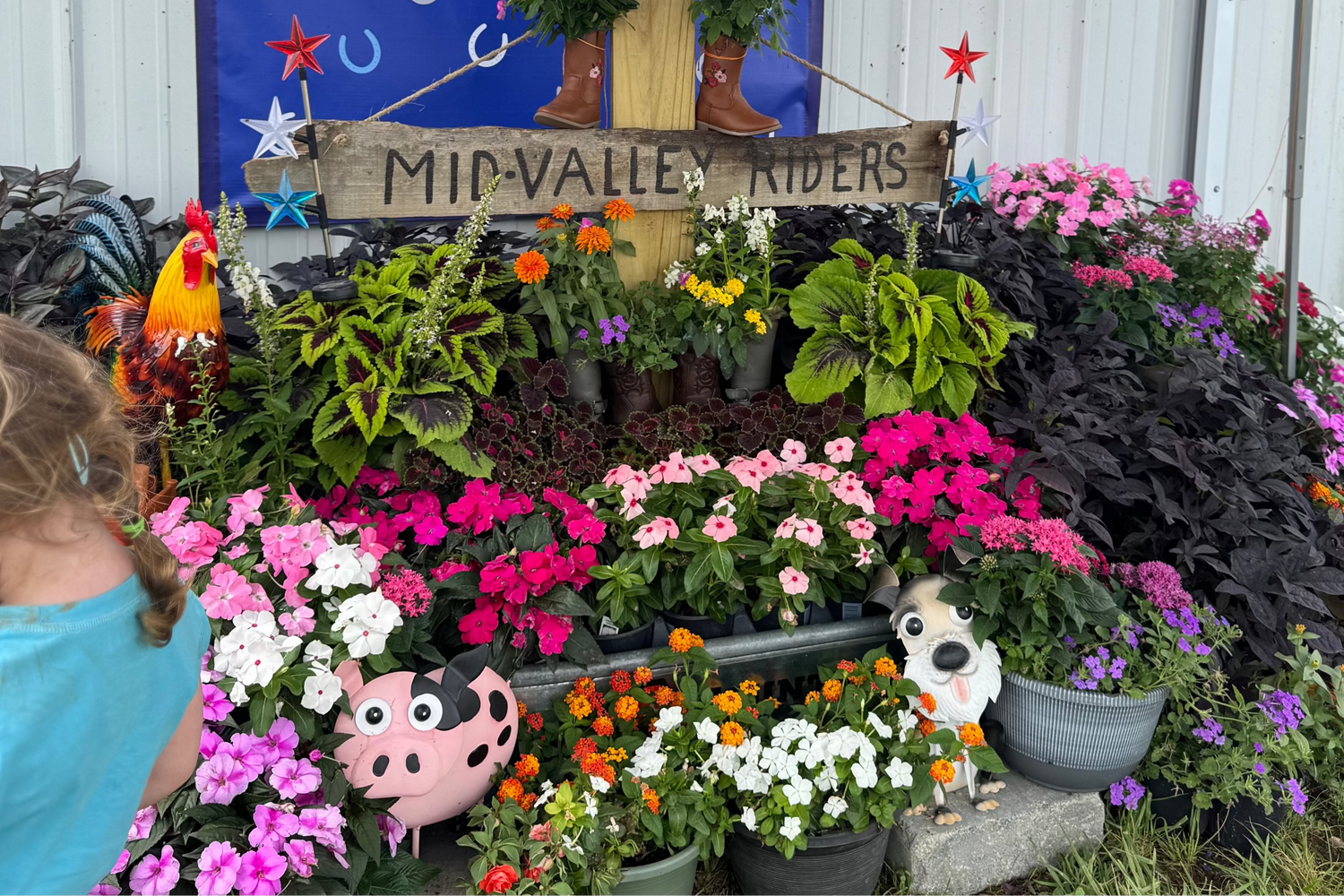 Blooming flowers outside barn with blue banner reads 'Mid Valley Riders' Local 4-H Club