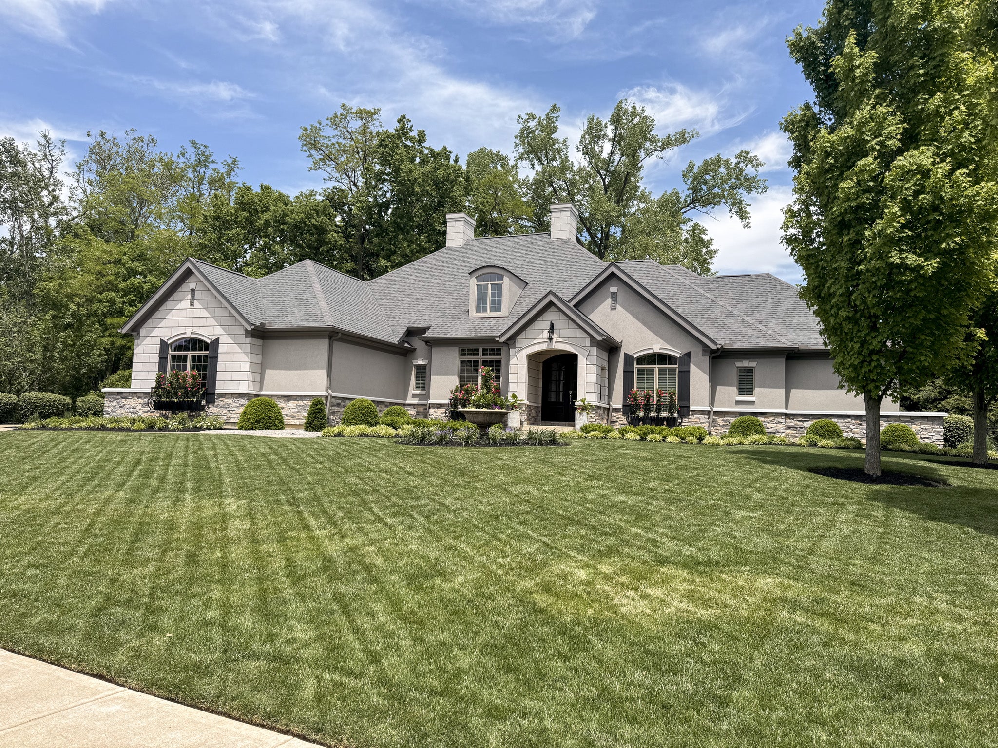 Stately house with a well-manicured lawn and trees under a blue sky.