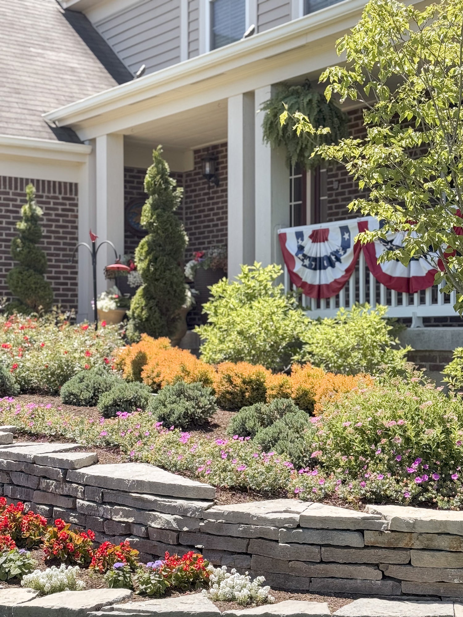 Front yard with garden, stone wall, and house with American flag banner