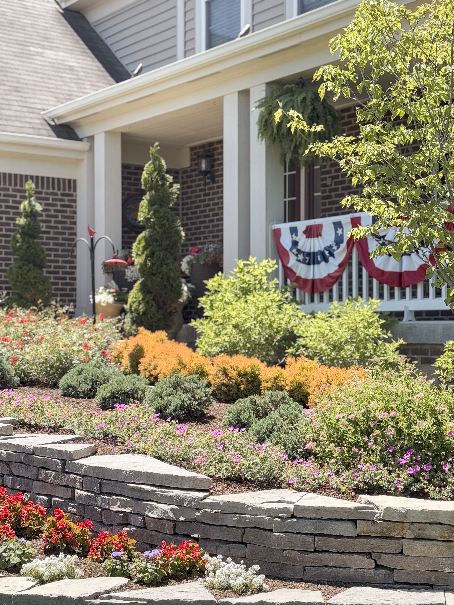Front yard with garden, stone wall, and house with American flag banner